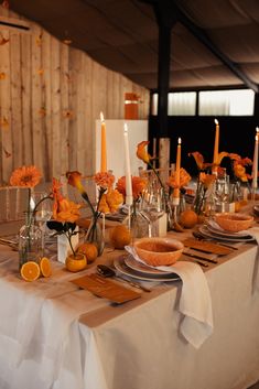 the table is set with oranges, candles and flowers in glass vases on it