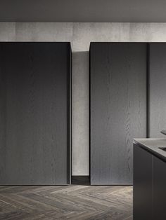 an empty kitchen with black cabinets and wood flooring on the walls, along with a sink