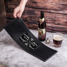 a person holding up a black mat with writing on it next to a glass of beer