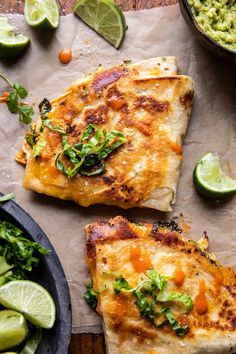 two quesadillas on parchment paper with limes and guacamole