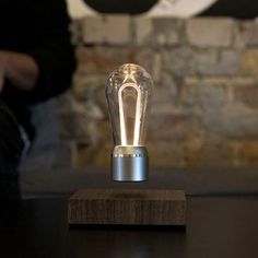 a light bulb sitting on top of a wooden table next to a person standing in front of a brick wall