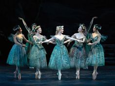 four ballerinas dressed in green tulle skirts and tiaras, with their arms outstretched