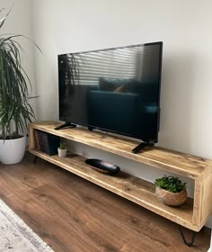 a flat screen tv sitting on top of a wooden shelf next to a potted plant