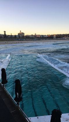 two people standing on the edge of a swimming pool near the ocean with waves coming in