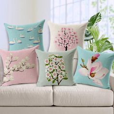 four pillows on a white couch with flowers and swans in the water, one is pink