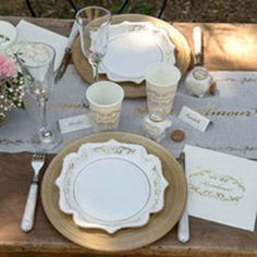 the table is set with white and gold plates, napkins, silverware, and flowers