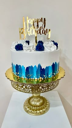 a white and blue birthday cake on a gold platter with the words happy birthday written on it