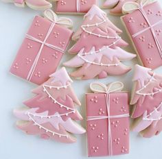 decorated cookies in the shape of christmas trees and presents on a white tablecloth with pink icing