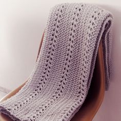 a crocheted blanket sitting on top of a wooden chair next to a white wall