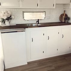 a kitchen with white cabinets and wood flooring in front of a mirror on the wall