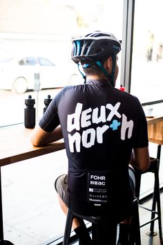 a man sitting at a table with a bike helmet on his head and wearing a jersey that says deux morh