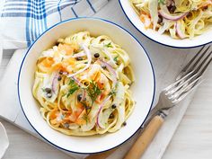 two bowls filled with pasta and vegetables on top of a wooden table next to utensils