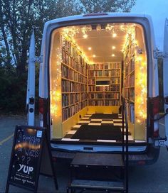 the back end of a van is decorated with fairy lights and bookshelves for display