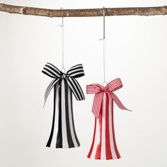 two christmas bells hanging from a tree branch with red and white ribbons tied to them