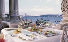 an outdoor dining area overlooking the water with white table cloths and place settings on it