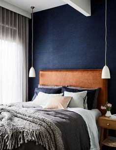 a bedroom with dark blue walls and white drapes on the windowsills, a large bed is flanked by two hanging lights