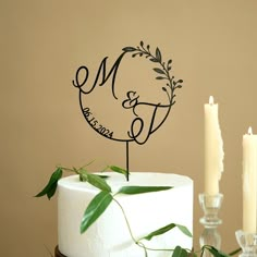 a cake with a monogrammed topper and two candles on the table next to it