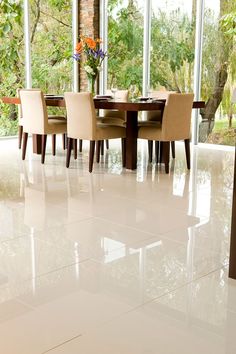 a dining room with large windows and white tile flooring on the walls, along with beige upholstered chairs