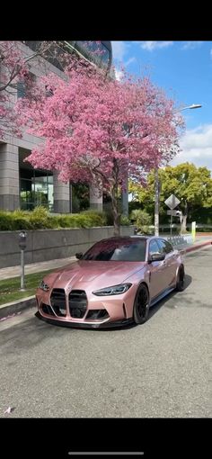 a pink car parked on the side of a road next to trees with pink flowers