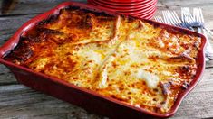 a red casserole dish with cheese on top and plates in the back ground