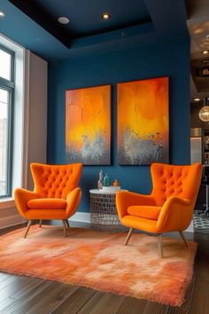 two orange chairs sitting in front of a painting on the wall next to a coffee table