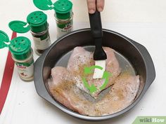 a person is cooking some meat in a frying pan with seasonings on the side