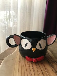 a black coffee cup with an owl's face painted on the side and eyes