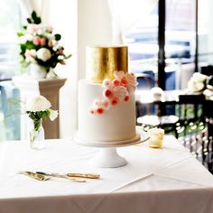 a white and gold wedding cake sitting on top of a table next to some flowers