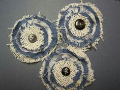 three blue and white fabric flowers with buttons on top of each flower, sitting on a gray surface