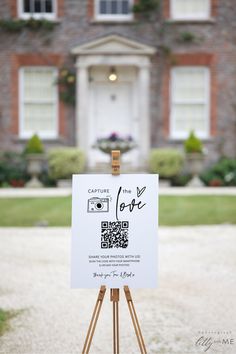 a white sign sitting on top of a wooden easel in front of a building