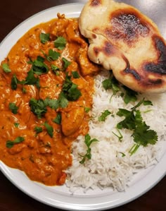 a white plate topped with rice and curry next to a piece of bread on top of a wooden table