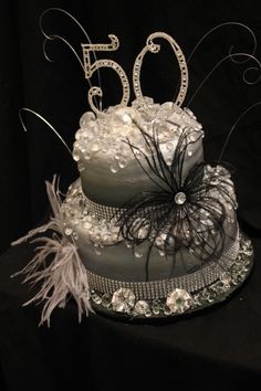 a 50th birthday cake decorated with feathers and beads on a black tableclothed background