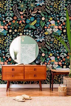 a dresser and mirror in front of a floral wallpapered room with plants on it