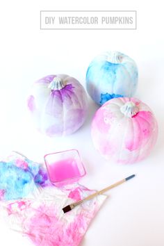 three painted pumpkins sitting on top of a table next to a container of liquid