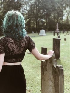 a woman with green hair standing in front of a grave yard and looking at the ground