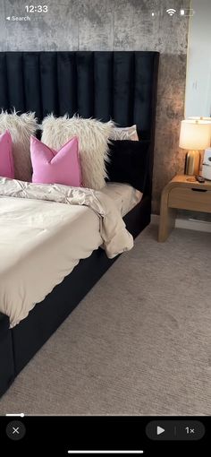 a bed with black headboard and pink pillows on it's sides, next to a night stand