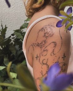 a woman with a tattoo on her arm next to some purple flowers and green leaves