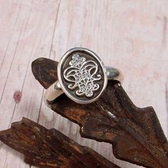 a silver ring sitting on top of a piece of wood with an intricate design in the middle