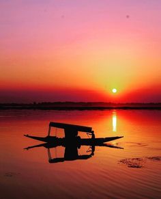 a boat sitting in the middle of a body of water under a colorful sky at sunset