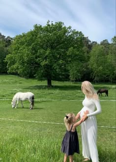 a woman and child standing in the grass near horses