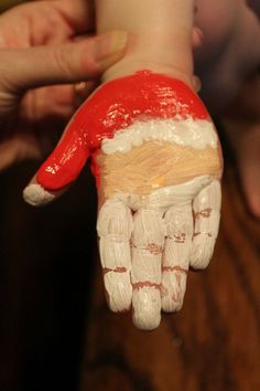 someone is holding out their hand with paint on it and santa's hat painted on the palm