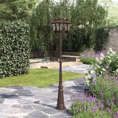 a lamp post in the middle of a garden with purple flowers and greenery around it