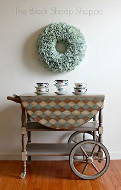 a wheelbarrow table with two cups on it and a wreath hanging over the top