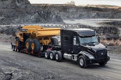 a dump truck driving down a dirt road next to a large rock formation in the background