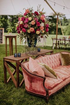 a pink couch sitting on top of a lush green field next to a wooden table