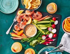 a platter with shrimp, carrots, celery, radishes and chips