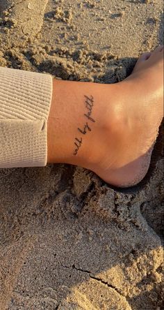 a person's foot in the sand with a small tattoo on their left leg