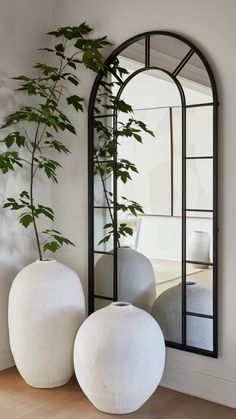 two white vases sitting on top of a wooden floor next to a large mirror