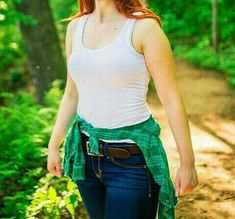 a woman with red hair is walking in the woods