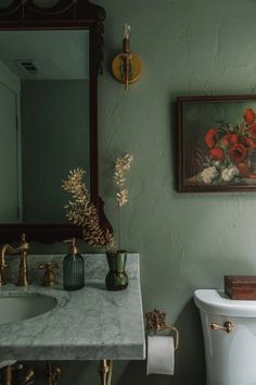 a bathroom with a sink, toilet and painting on the wall in it's corner